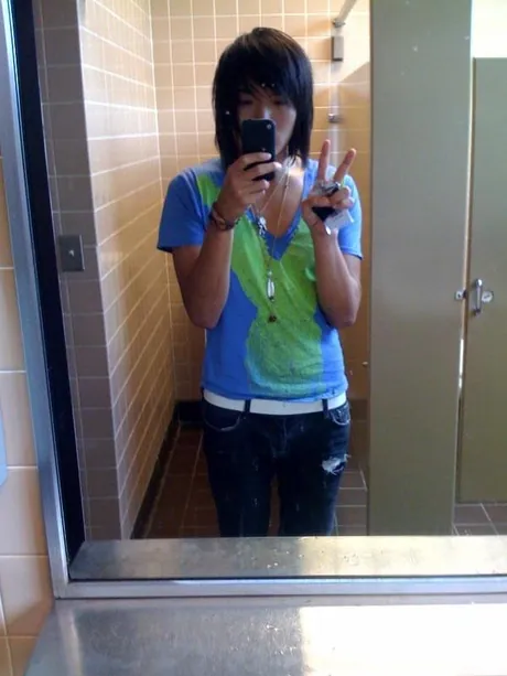 Jason as a teenager taking a mirror selfie in a tiled bathroom, the original iPhone held up in one hand and a peace sign in the other